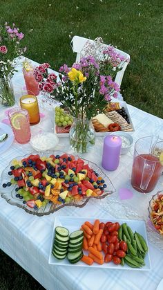 a table topped with lots of food and drinks on top of a grass covered field