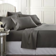 a bed with grey sheets and pillows on it