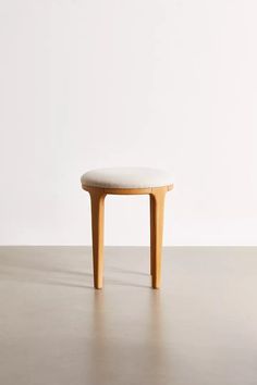 a small wooden stool sitting on top of a cement floor next to a white wall