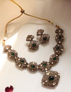 Inspired by the romantic Victorian era, this elegant necklace set is a true masterpiece. Encrusted with sparkling polki stones and adorned with cubic zirconia for added brilliance, it features emerald green stones that add a touch of color and allure. Accompanied by matching earrings, this set is the perfect choice for a formal occasion, exuding timeless charm and sophistication. Finish: Rhodium Plating Material: Silver, Copper Alloy, Emerald, Polki & CZs Color: Green Size: Free Size, Adjustable Elegant Hand-set Emerald Necklace For Reception, Elegant Hand Set Emerald Necklace For Reception, Elegant Silver Emerald Necklace With Stone Work, Elegant Silver Kundan Necklace With Emerald, Elegant Emerald Kundan Necklace For Gift, Green Diamond Necklaces With Rose Cut, Green Diamond Necklaces With Rose Cut Diamonds, Green Emerald Jewelry With Rose Cut Diamonds, Elegant Jeweled Green Emerald Necklace