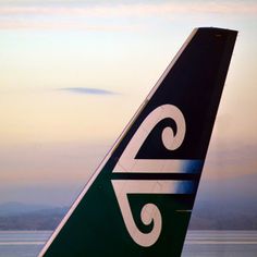 the tail end of an airliner that is green and white with swirls on it