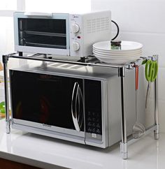 two microwaves are stacked on top of each other in the kitchen counter with plates and utensils