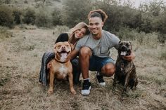 a man and woman sitting on the ground with two dogs in front of them smiling at the camera