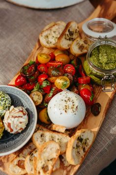 an assortment of food is displayed on a wooden platter with bread and pesto