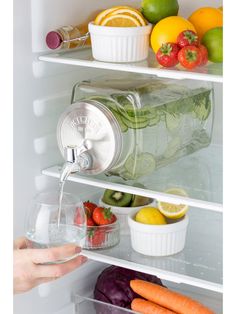 a refrigerator filled with lots of fresh fruits and vegetables next to a person pouring water