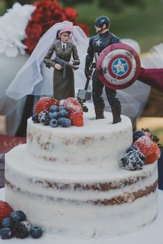 two figurines on top of a cake with berries and strawberries around it