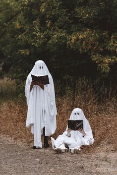 two people dressed as ghost reading books in the grass with trees behind them and bushes