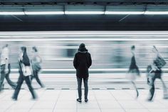 a man standing in front of a train station with blurry people on the platform