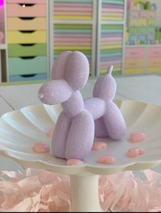 a pink poodle sitting on top of a white cake plate next to other items