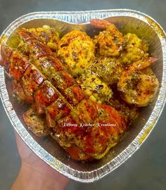 a hand holding a foil container filled with cooked shrimp