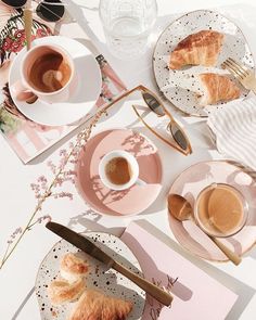 two cups of coffee and croissants are on the table with pink napkins