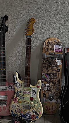 two guitars are sitting next to each other with stickers all over them on the wall