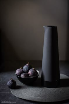 a black vase sitting on top of a table next to some figs