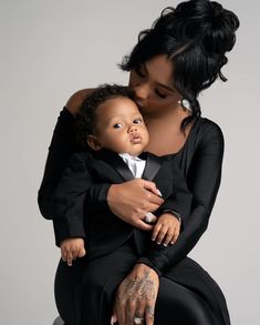 a woman holding a baby in her arms and looking at the camera while she is wearing a tuxedo