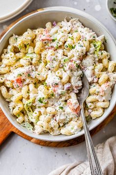 a white bowl filled with pasta salad next to a wooden spoon on top of a table