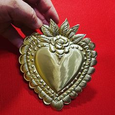 a gold heart shaped brooch sitting on top of a red cloth covered table next to a person's hand