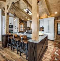 a kitchen with an island and bar stools in the center, surrounded by wooden beams