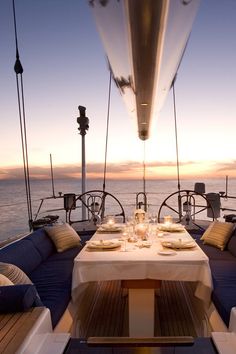 the dining table is set up on the deck of a boat at sunset or dawn