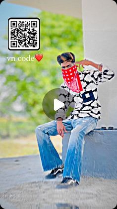 a young man sitting on top of a cement wall wearing jeans and a red bandana