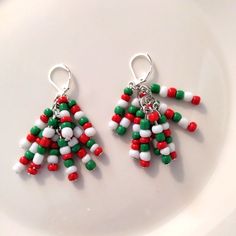 two red, white and green beaded christmas tree earrings sitting on top of a plate