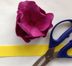 a pair of blue scissors next to a pink flower on a yellow ribbon with the end cut off