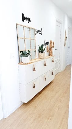 a white dresser sitting next to a wall with some plants on top of it in front of a mirror