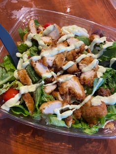 a salad in a plastic container with dressing on top and a fork next to it