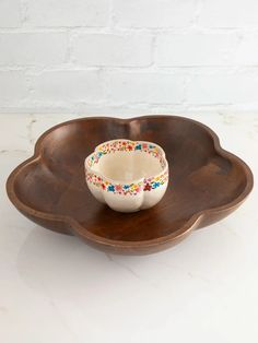 a wooden bowl with flowers painted on the rim sits in front of a white brick wall