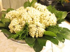 a vase filled with lots of white flowers on top of a table covered in greenery