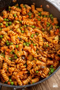 a pan filled with pasta and peas on top of a wooden table