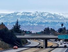 a highway with mountains in the background and cars driving on it's side,