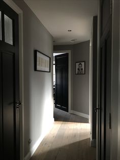 an empty hallway with two black doors and pictures on the wall above it, along with hardwood flooring