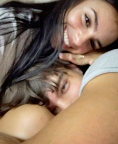 two women are laying in bed together and smiling at the camera, with one woman's head resting on her shoulder