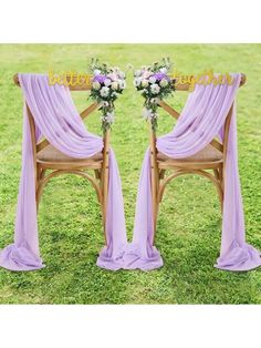 two wooden chairs with purple drapes and flowers on them, sitting in the grass