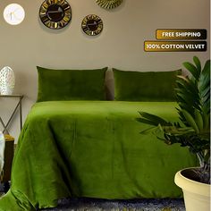 a bed with green sheets and pillows next to a potted plant on the floor