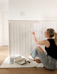 a woman sitting on the floor painting a wall