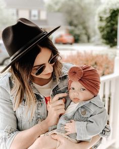 a woman holding a baby in her arms and wearing a hat on top of her head