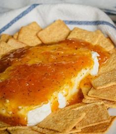 a plate filled with cheese and crackers on top of a white cloth next to some chips