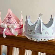 two princess crowns sitting on top of a wooden table next to each other, one pink and one blue