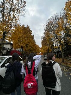 three girls walking down the street with backpacks on their back and one girl holding her hand up