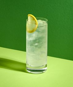 a glass filled with ice and lemon on top of a green table next to an orange slice