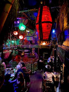 several people sitting at tables in a room with lights hanging from the ceiling and decorations on the walls