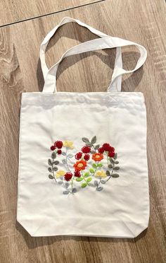 a white bag with flowers painted on it sitting on a wooden floor next to a pair of scissors