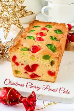 a loaf of christmas cherry pound cake on a white platter next to a red ornament