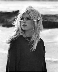 a black and white photo of a woman standing on the beach with her hair blowing in the wind