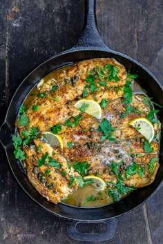 a skillet filled with chicken and lemons on top of a wooden table next to a