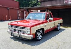 a red and tan truck parked in front of a storage building with two garage doors