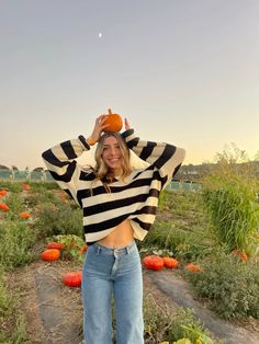 a woman standing in a pumpkin patch with her hands on her head