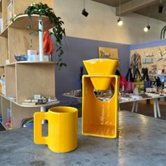 two yellow coffee mugs sitting on top of a counter in a room filled with tables and chairs