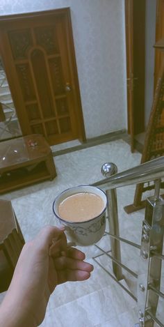 a person holding a cup of coffee on top of a glass railing in a living room